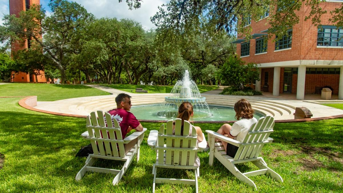 Students sitting in Adirondack chairs next to a fountain